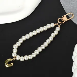 Detailed macro shot of white pearl phone lanyard featuring a gold-plated letter U charm