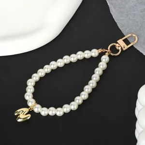 Close-up of elegant pearl phone strap with gold-tone letter M charm on black background