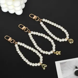Detailed view of three white pearl keychains with gold-plated clasps and initial charms