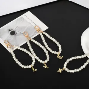 Detailed macro view of white imitation pearl phone chains featuring gold-plated letter charms