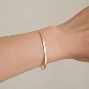 Close-up view of a minimalist gold herringbone snake chain bracelet worn on a person's wrist.