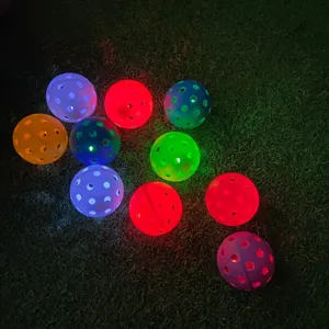 Close-up view of glowing LED pickleballs with 40 holes displayed on grass at night.