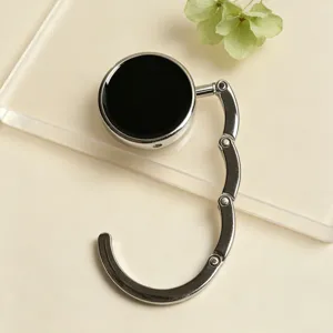 Close-up view of a portable silver metal bag hook with a glossy black round decorative top