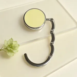 Detailed close-up of a portable foldable handbag hook with a pale yellow top disc