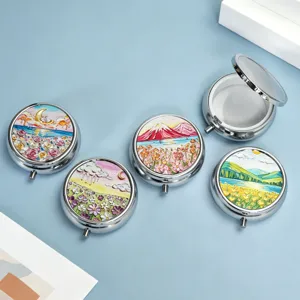 Set of five round silver pillboxes with colorful landscape prints on light blue surface