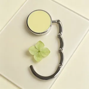 Minimalist portable silver table hook for bags with a pastel yellow circular top