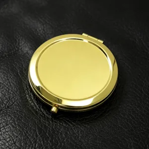 Elegante ronde gouden metalen draagbare zakmake-upspiegel op zwart lederen oppervlak