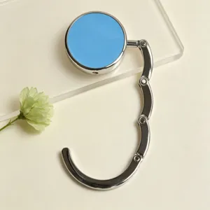 Detailed view of a portable foldable bag hook with a blue finish on a minimalist desk