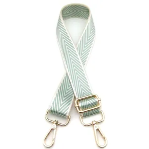 Detalle de correa ajustable para bolso con patrón de flechas verdes y herrajes dorados
