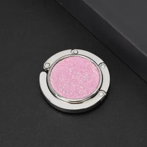 Close-up of a circular folding handbag hook with a pink glitter center on a dark background