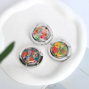 Detailed view of three foldable metal handbag hooks with colorful tropical floral patterns