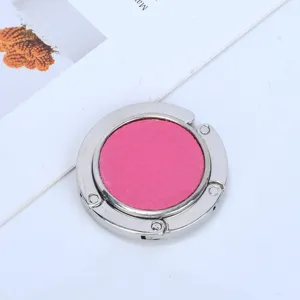 Macro view of a foldable round metal purse hook with pink leather inlay for desk.