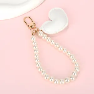 Close-up van een wit lederen hartje en een elegante parelketting sleutelhanger met goud