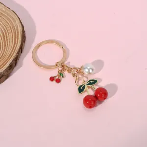 Macro detail of red resin cherry and white pearl charms on golden metal keychain