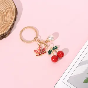 Detailed view of red cherry and maple leaf charms on a golden metal keychain.