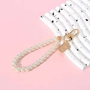 Close-up of elegant pearl chain keychain with golden coin pendant on pink background
