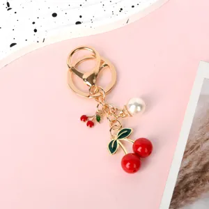 Detailed view of the red resin cherry and pearl charms on the golden keychain