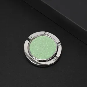 Close-up detail of a circular silver folding bag hook with vibrant green glitter inlay