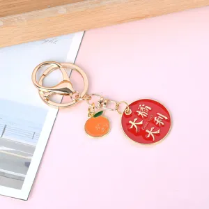 Detail shot of a golden metal keychain featuring an orange charm and a lucky red disk