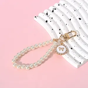 Detailed view of pearl phone charm strap with golden bow pendant and metal clasp