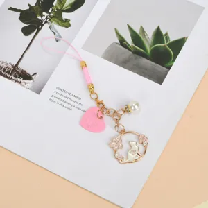 Detailed view of a cute white cat phone strap featuring cherry blossom and pearl accents