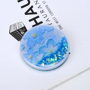 Close-up of portable round makeup mirror with blue floral quicksand glitter effect.