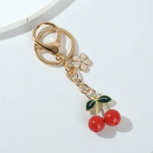 Detailed macro view of vibrant red resin cherry and flower charms on a golden keychain.