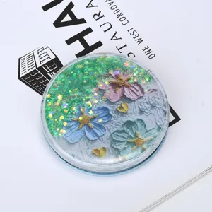 Close-up detail of a round quicksand makeup mirror with green glitter and floral motifs.