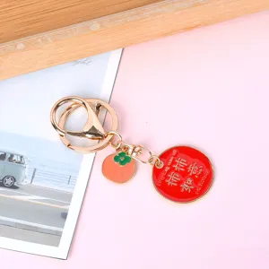 Close-up of a gold-plated keychain with a red lucky charm and persimmon pendant