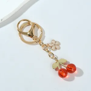 Macro detail of red resin cherry and white enamel flower charms on a gold keychain