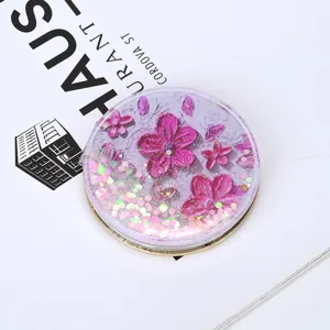 Macro view of portable quicksand makeup mirror with pink flowers and floating sequins.