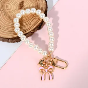Close-up of pearl bead strap with pink bow charm and gold heart pendant for bags.