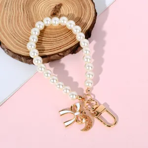 Close-up detail of pearl phone strap featuring elegant bow and crescent moon charms.