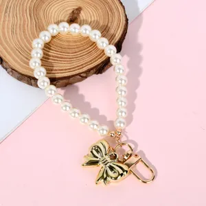 Elegant pearl keychain with a gold-tone bow charm and sturdy metal clasp close-up view.