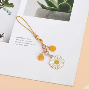 Detail view of a cute daisy flower and yellow smiley face charms on a golden phone strap