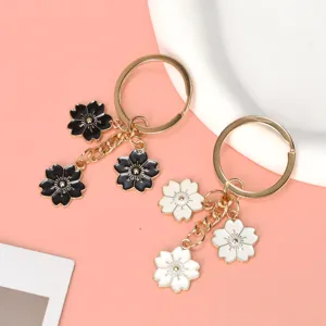 Close-up view of black and white enamel cherry blossom metal keychains on pink background
