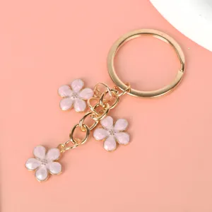 Close-up detail of pink enamel sakura flower charms on a golden metal keychain ring