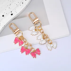 Close-up of pink and white enamel bow-knot keychains with gold-toned chains