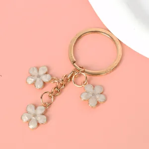 Detail of gold-tone metal keychain with three white cherry blossom flower charms.