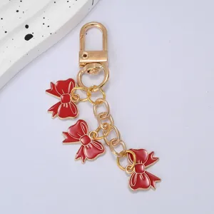 Close-up view of a gold-plated keychain featuring three vibrant red enamel bow pendants.