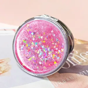 Close-up view of portable pink quicksand makeup mirror with heart-shaped holographic glitter