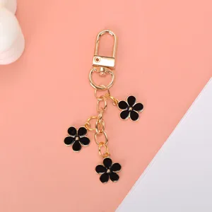 Close-up view of golden alloy keychain featuring three elegant black enamel flower charms.