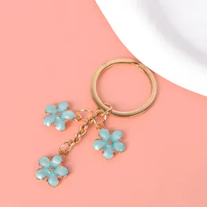 Close-up of gold metal keychain featuring three light blue enamel cherry blossom charms