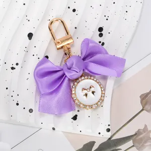 Elegant purple satin bow keychain featuring a detailed pearl and rhinestone medallion