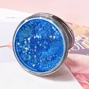 Detailed view of the sparkling blue quicksand cover on a round folding makeup mirror.