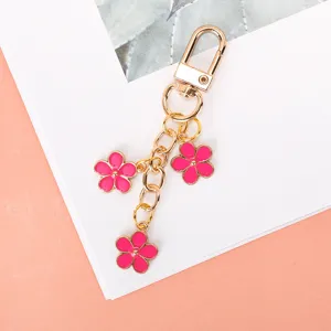 Close-up of golden keychain featuring three pink enamel flower charms for bags