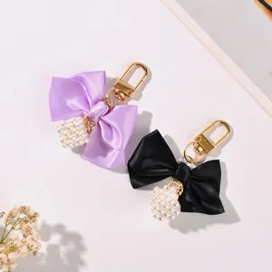 Detailed view of ribbon bow keychains with pearl cube charms and gold hardware.