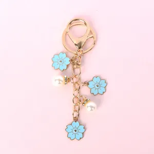 Detalle de dijes de sakura azul claro y perlas blancas en un llavero de tono dorado