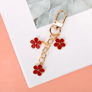 Delicate golden keychain featuring three red enamel flower charms for bags and keys
