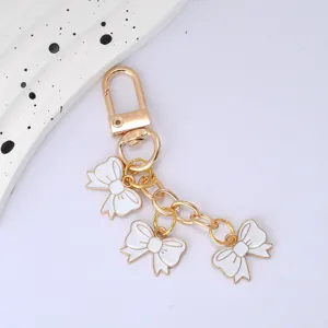 Detail view of gold keychain with three white enamel bow charms for bag decoration